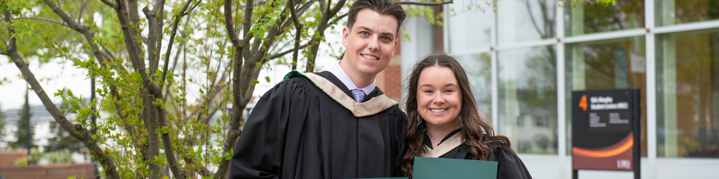 two ͯŮ graduates holding their degrees